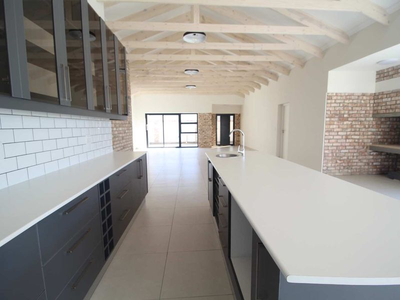 Spacious open-plan kitchen and living area featuring modern cabinetry, a large island, exposed timber trusses, and rustic brick accents.