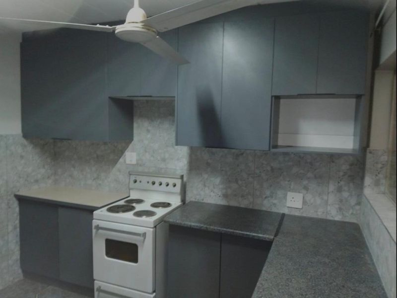 A functional kitchen featuring dark grey cabinetry, stone-look tiled backsplash, laminate countertops, and a freestanding stove.