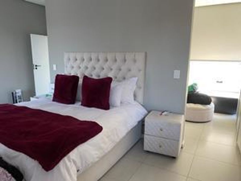 A well-maintained bedroom featuring neutral wall tones, tiled flooring, and integrated lighting, with an adjoining space visible through the doorway.