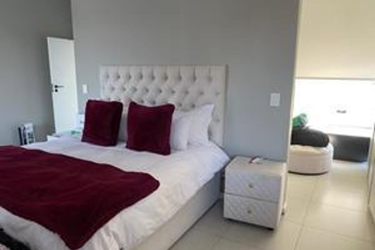 A well-maintained bedroom featuring neutral wall tones, tiled flooring, and integrated lighting, with an adjoining space visible through the doorway.