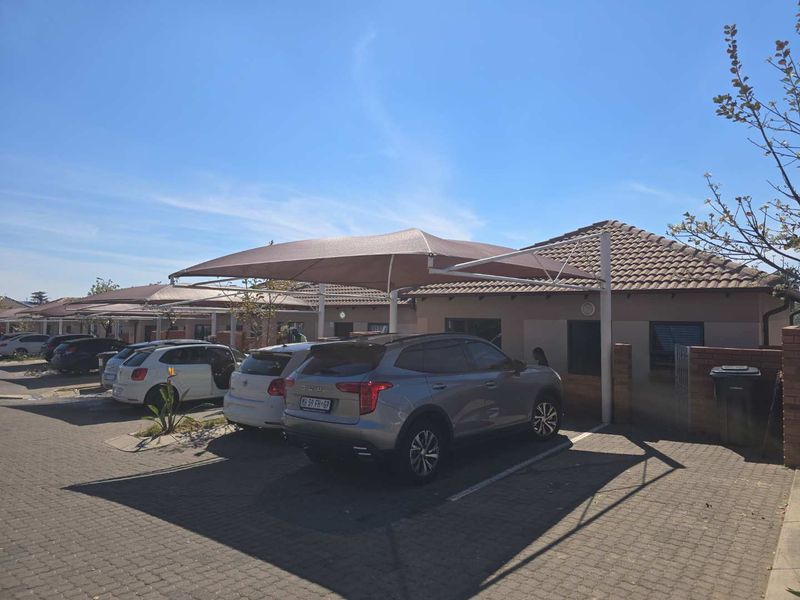 Front exterior view of the property featuring a paved driveway and covered shade cloth carports.