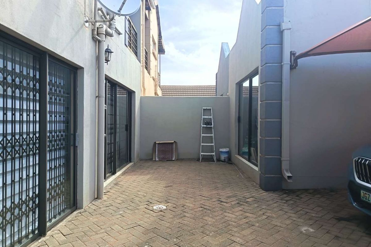 A paved rear courtyard area featuring sliding glass doors with security gates, downpipes, and an exterior wall-mounted satellite dish.