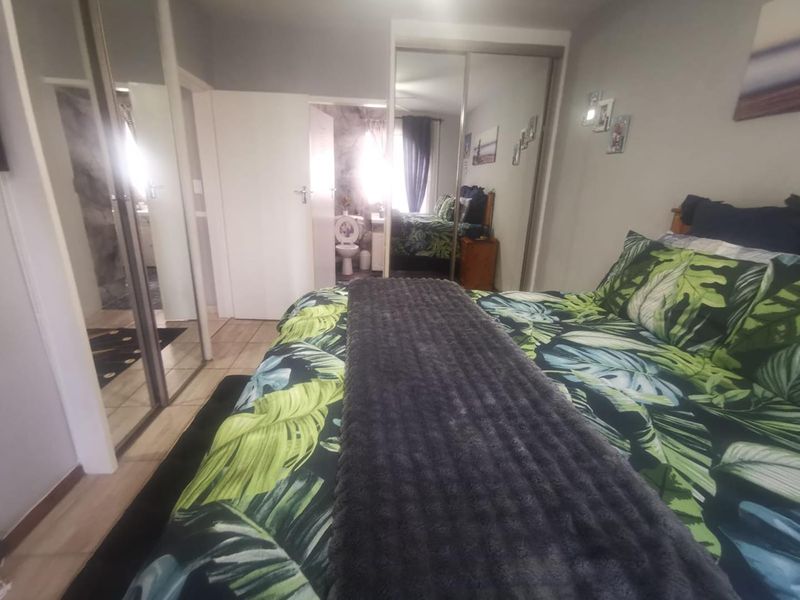 Bedroom featuring built-in cupboards with mirrored sliding doors, tiled flooring, and direct access to an en-suite bathroom.