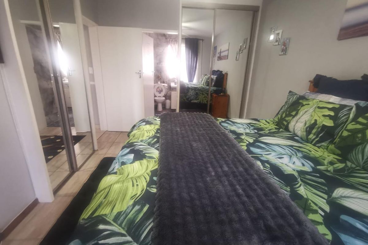 Bedroom featuring built-in cupboards with mirrored sliding doors, tiled flooring, and direct access to an en-suite bathroom.