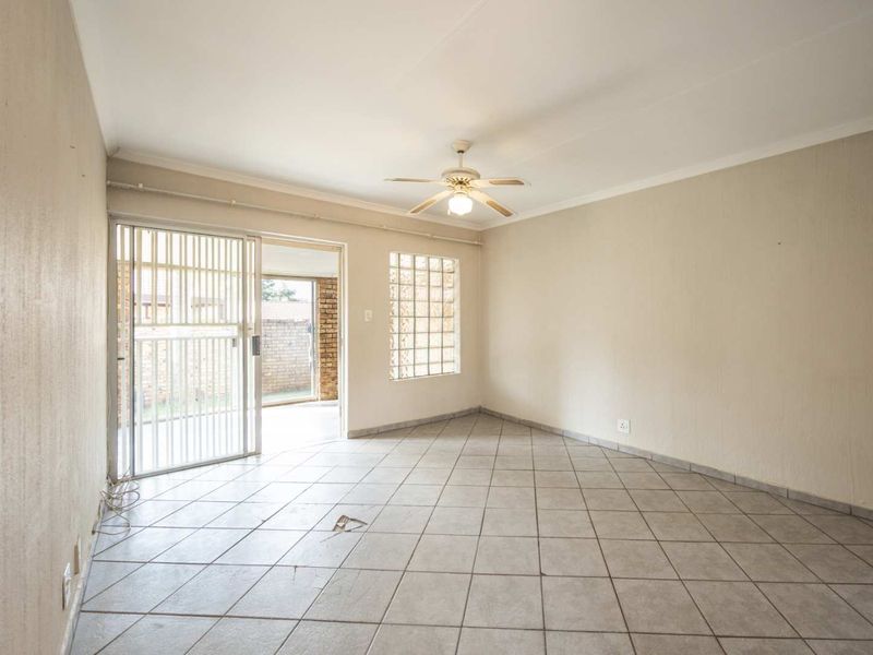 An empty living room featuring tiled flooring, a ceiling fan, and a security gate leading to an outdoor area.