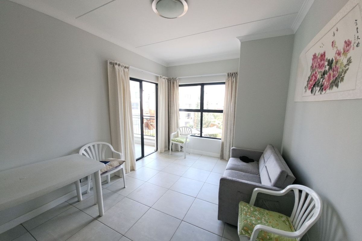 A bright living area featuring neutral tiled flooring, large windows, and a sliding door providing access to an outdoor balcony space.