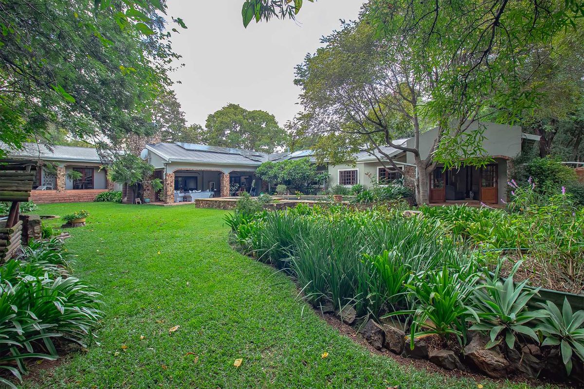 Spacious rear garden featuring a lush lawn, mature trees, and a covered patio area connected to the main residence.