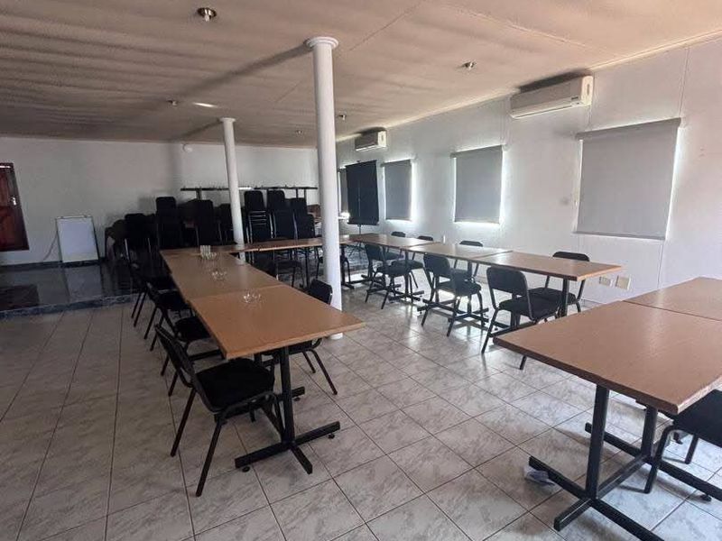 Spacious office or meeting area featuring tiled flooring, structural support columns, wall-mounted air conditioning units, and functional roller blinds.