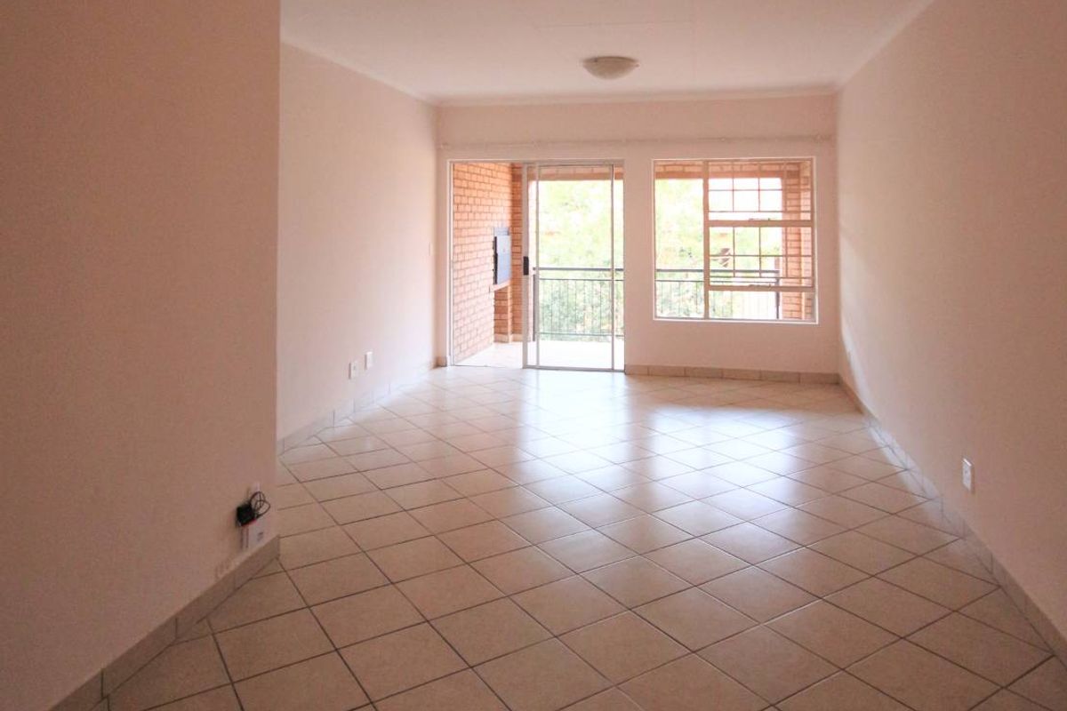A spacious, empty living room featuring neutral tiled flooring, natural light from a large window, and access to an outdoor balcony area.