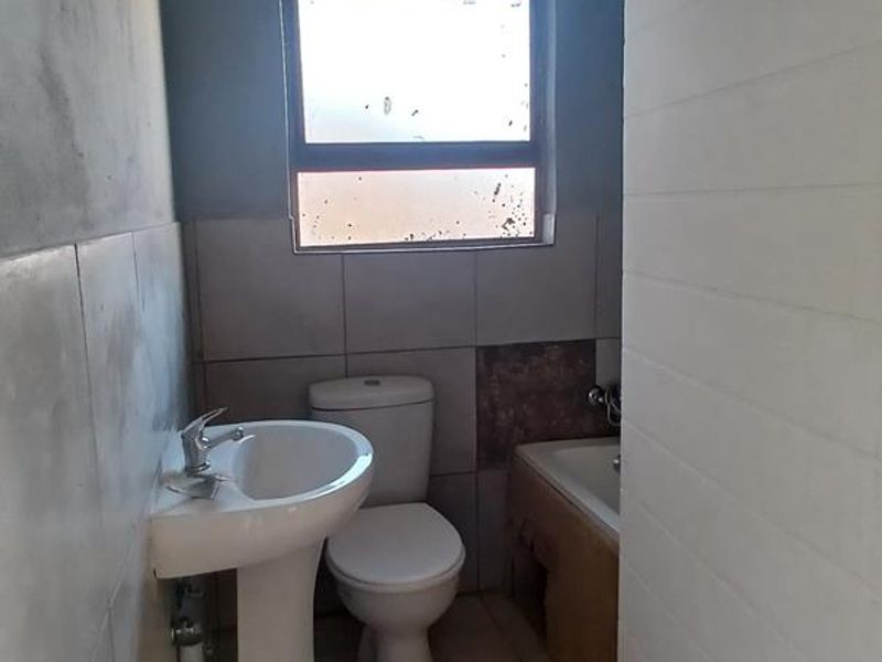 A compact bathroom featuring a pedestal basin, toilet, and bathtub, currently requiring finishing touches to the wall plaster and tiling.