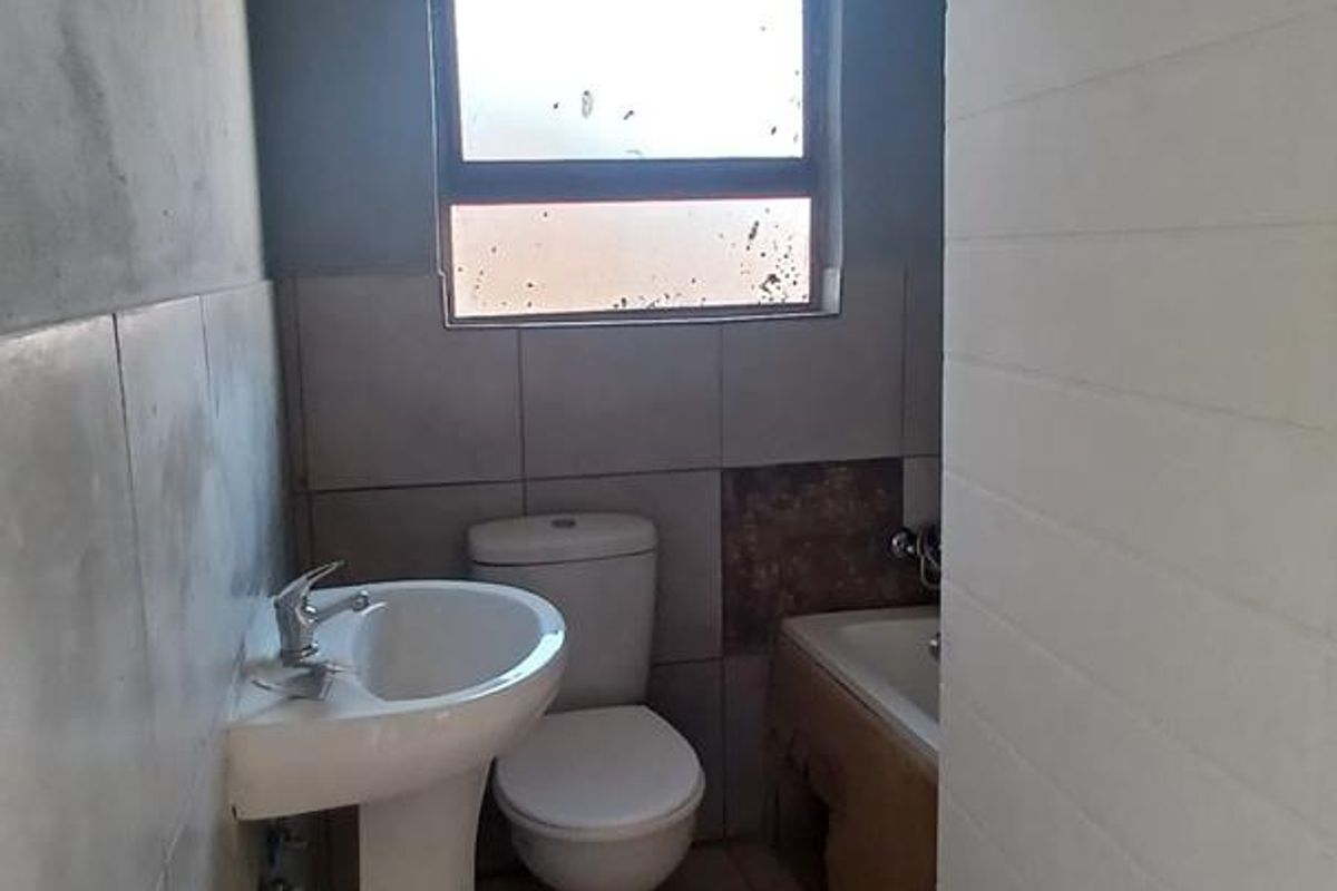 A compact bathroom featuring a pedestal basin, toilet, and bathtub, currently requiring finishing touches to the wall plaster and tiling.