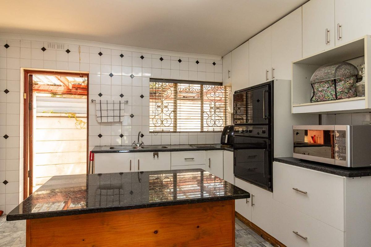 A functional kitchen featuring white cabinetry, dark granite countertops, a central island, and a built-in oven, with direct access to an outdoor area.