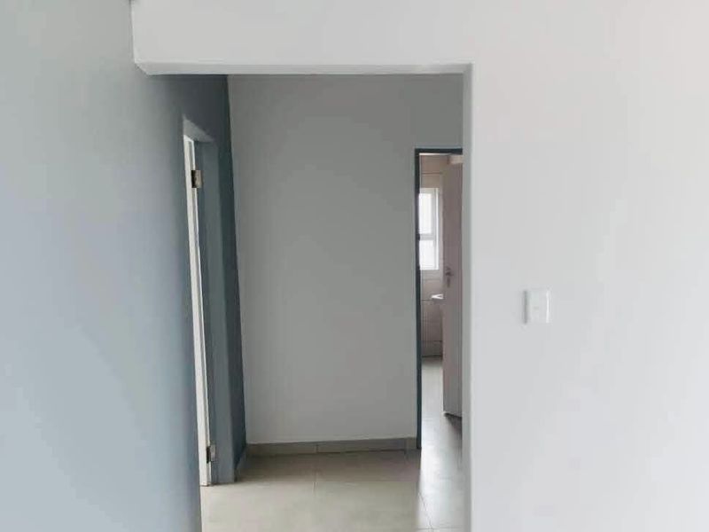 A clean, neutral-toned hallway connecting multiple rooms, featuring tiled flooring and simple architectural finishes.
