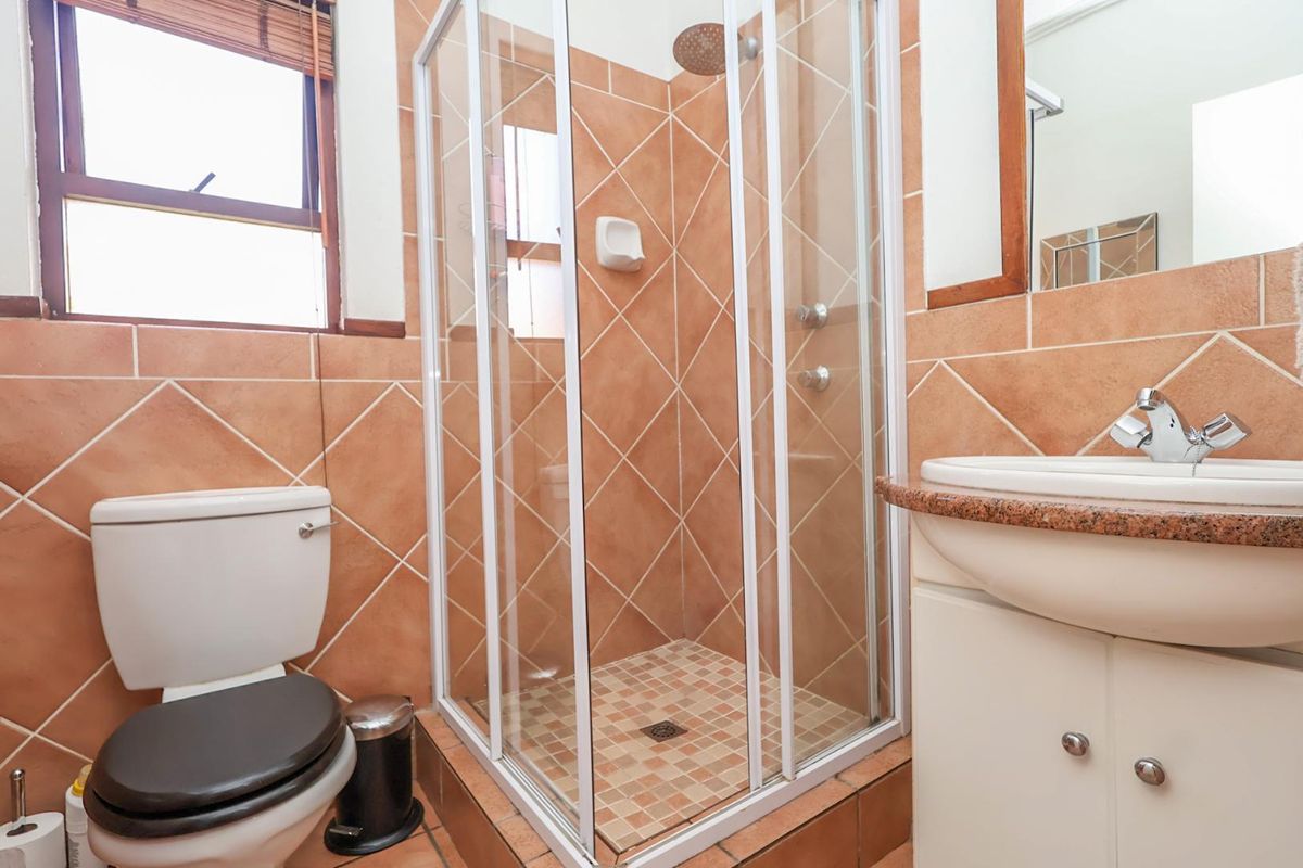 A functional bathroom featuring a shower enclosure, toilet, and vanity basin with tiled finishes throughout.