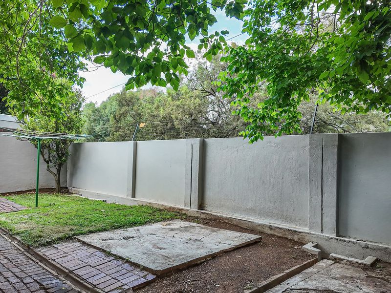 A private rear garden area featuring a perimeter wall with electric fencing, brick paving, and a concrete slab foundation.