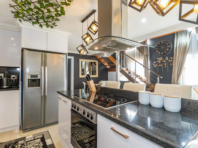 Modern open-plan kitchen featuring granite countertops, gloss cabinetry, and integrated appliances, seamlessly flowing into the living area with a feature staircase.