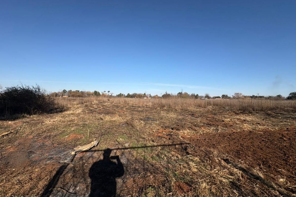 A view of a vacant residential plot featuring cleared land and natural vegetation under a clear blue sky.