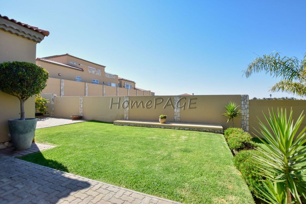 A well-maintained rear garden featuring a manicured lawn, paved patio area, and a decorative stone-accented boundary wall.