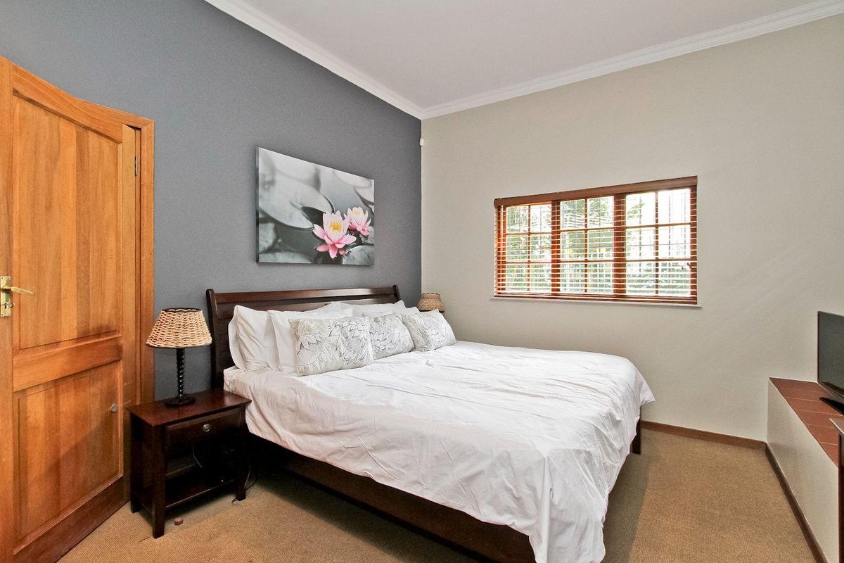 A well-maintained bedroom featuring neutral walls, a grey accent wall, carpeted flooring, and wooden window blinds.