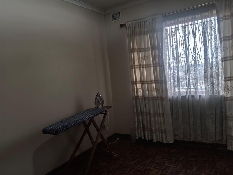 A simple bedroom featuring parquet flooring and a window with curtains, offering a blank canvas for personalization.