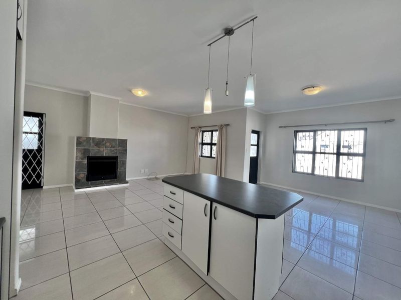 Spacious open-plan living area featuring tiled flooring, a central kitchen island, and a fireplace with a tiled surround, offering a bright and versatile layout.