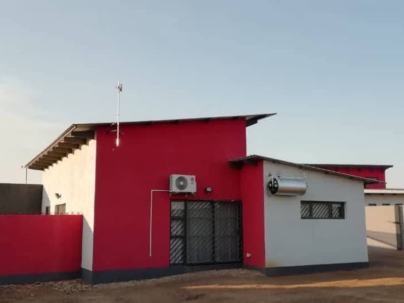 Rear view of a modern house featuring a bold red and white facade, solar geyser, and secure gated access.