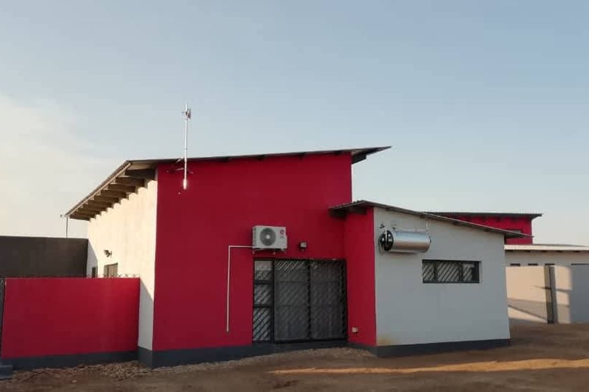 Rear view of a modern house featuring a bold red and white facade, solar geyser, and secure gated access.
