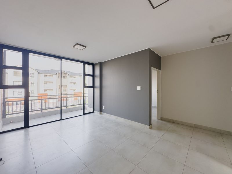 A bright, empty living area featuring large sliding glass doors, neutral tiled flooring, and a modern grey accent wall.