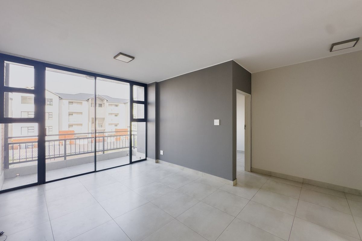 A bright, empty living area featuring large sliding glass doors, neutral tiled flooring, and a modern grey accent wall.