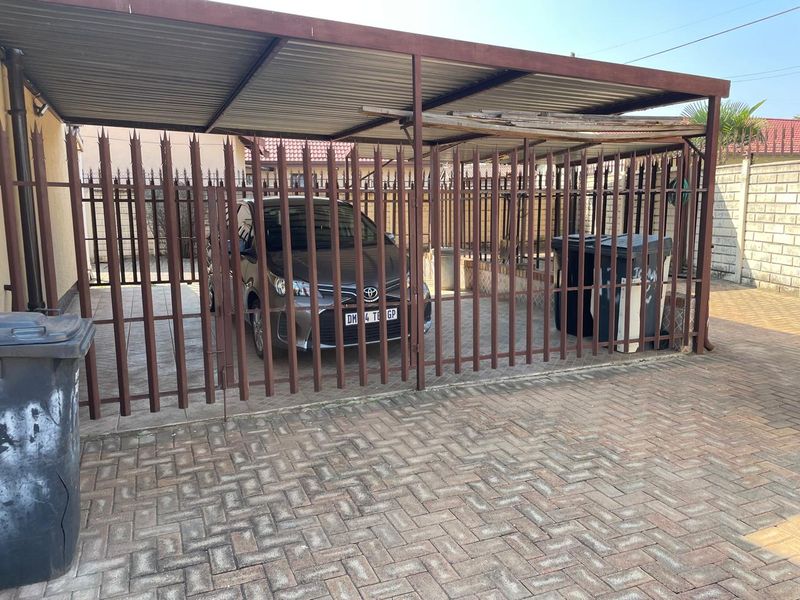 A covered carport area featuring steel security fencing and paved flooring, showing signs of wear on the roof structure.