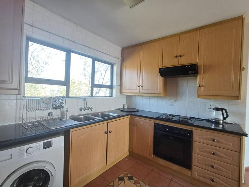 A functional kitchen featuring wooden cabinetry, dark countertops, a built-in oven with hob, and a double sink under a large window.