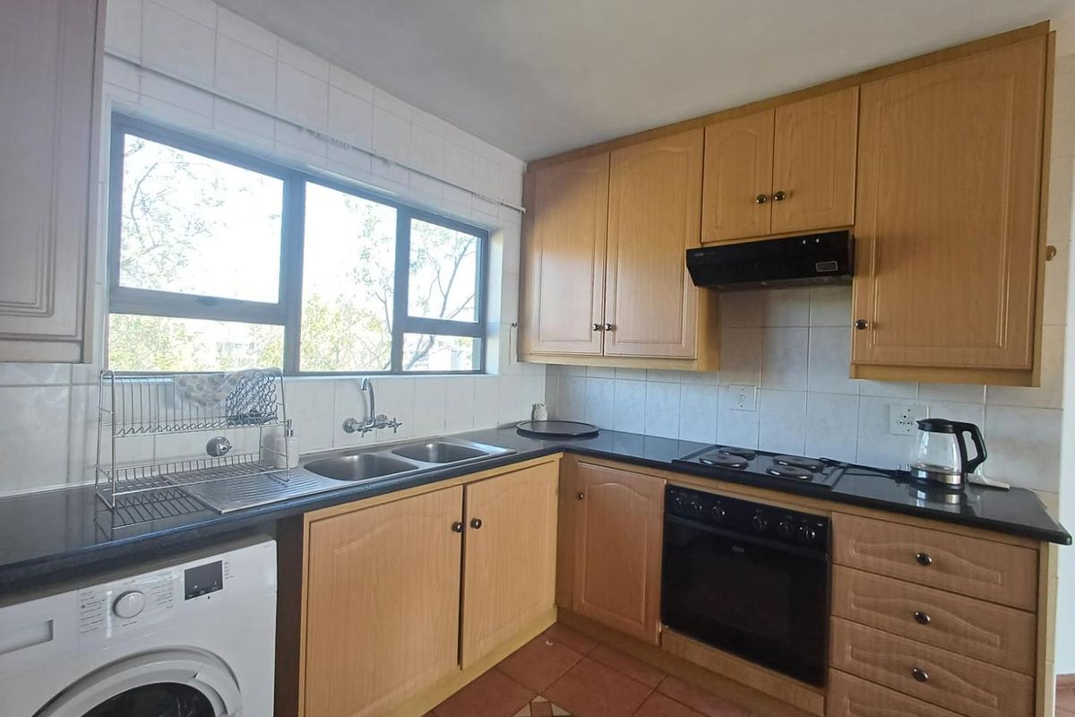 A functional kitchen featuring wooden cabinetry, dark countertops, a built-in oven with hob, and a double sink under a large window.