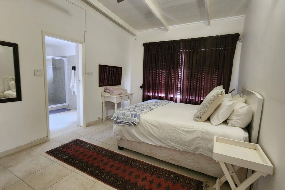 A bedroom featuring tiled flooring, exposed beam ceilings, and direct access to an en-suite bathroom.