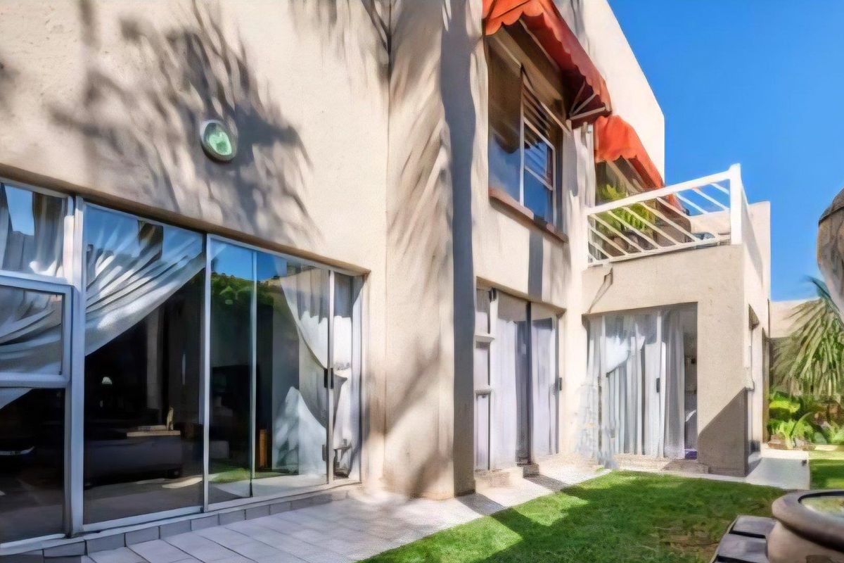 Rear view of the cluster property featuring a paved patio, garden area, sliding glass doors, and an upper-level balcony with red awnings.