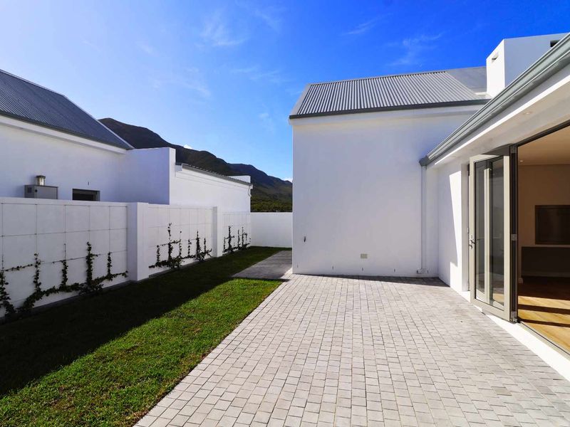 A modern rear exterior featuring a paved patio, manicured lawn, and bi-fold doors leading into the home, set against a mountain backdrop.