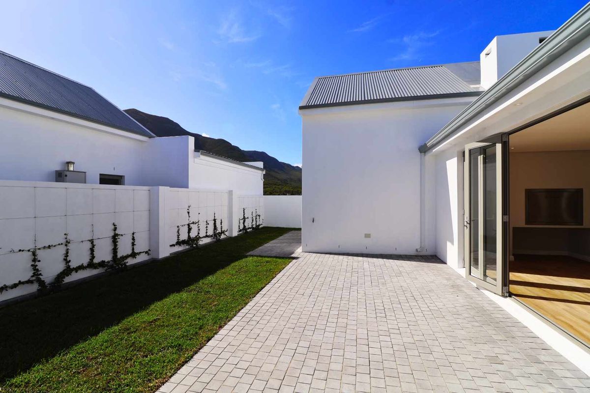 A modern rear exterior featuring a paved patio, manicured lawn, and bi-fold doors leading into the home, set against a mountain backdrop.
