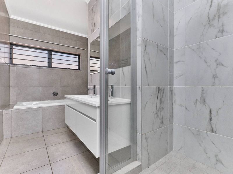 Modern bathroom featuring a sleek double vanity, a built-in bathtub, and a separate glass-enclosed shower with contemporary marble-look and grey tiling.