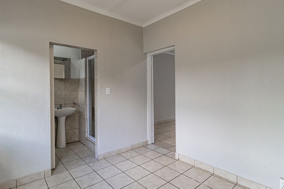 An empty bedroom featuring tiled flooring and an en-suite bathroom with a pedestal basin and shower enclosure.