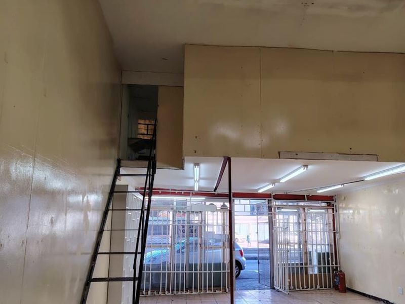 Empty commercial utility space featuring tiled flooring, a metal staircase leading to a mezzanine level, and secure metal gate entrance.