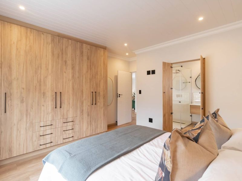 Modern bedroom featuring extensive built-in timber-look cabinetry, recessed lighting, and a convenient en-suite bathroom with a glass-enclosed shower.