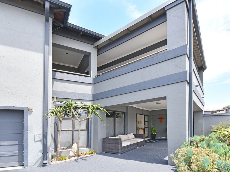 Front elevation of a modern double-story house featuring a covered ground-floor patio, upper-level balcony, and paved entrance area.