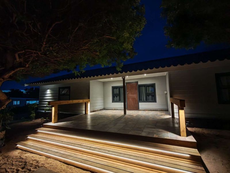 A well-lit covered patio featuring tiled flooring, timber decking steps with integrated LED lighting, and timber handrails, creating an inviting outdoor entrance area.