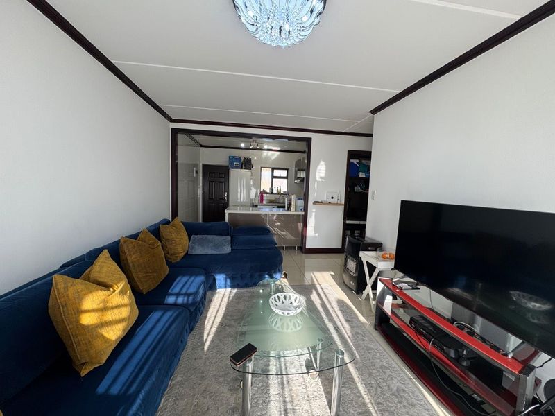 An open-plan living area featuring tiled flooring, crown molding, and a crystal chandelier, with a view into the adjacent kitchen space.