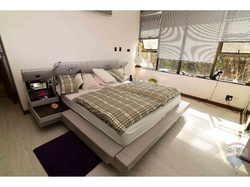 A bedroom featuring large windows with fitted blinds, light-toned flooring, and a wall-mounted air conditioning unit.