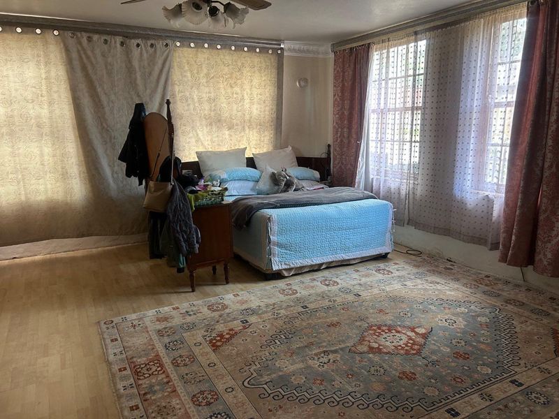Spacious bedroom featuring light-toned laminate flooring, decorative ceiling molding, and large windows with natural light.