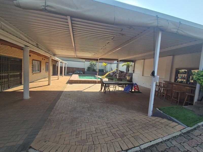 Spacious covered patio area featuring brick paving, a built-in bar, and direct access to an outdoor swimming pool.