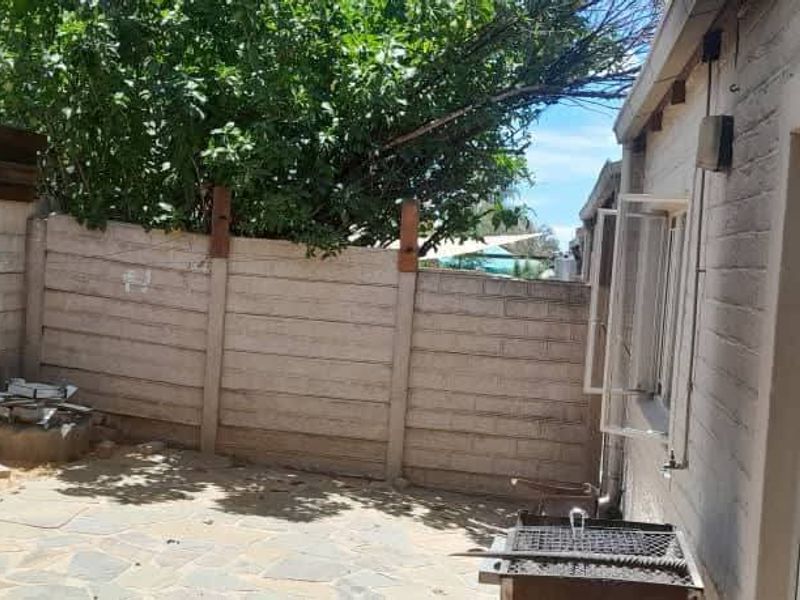 A private rear courtyard featuring a paved patio area, enclosed by precast concrete boundary walls and accessible via a sliding glass door.
