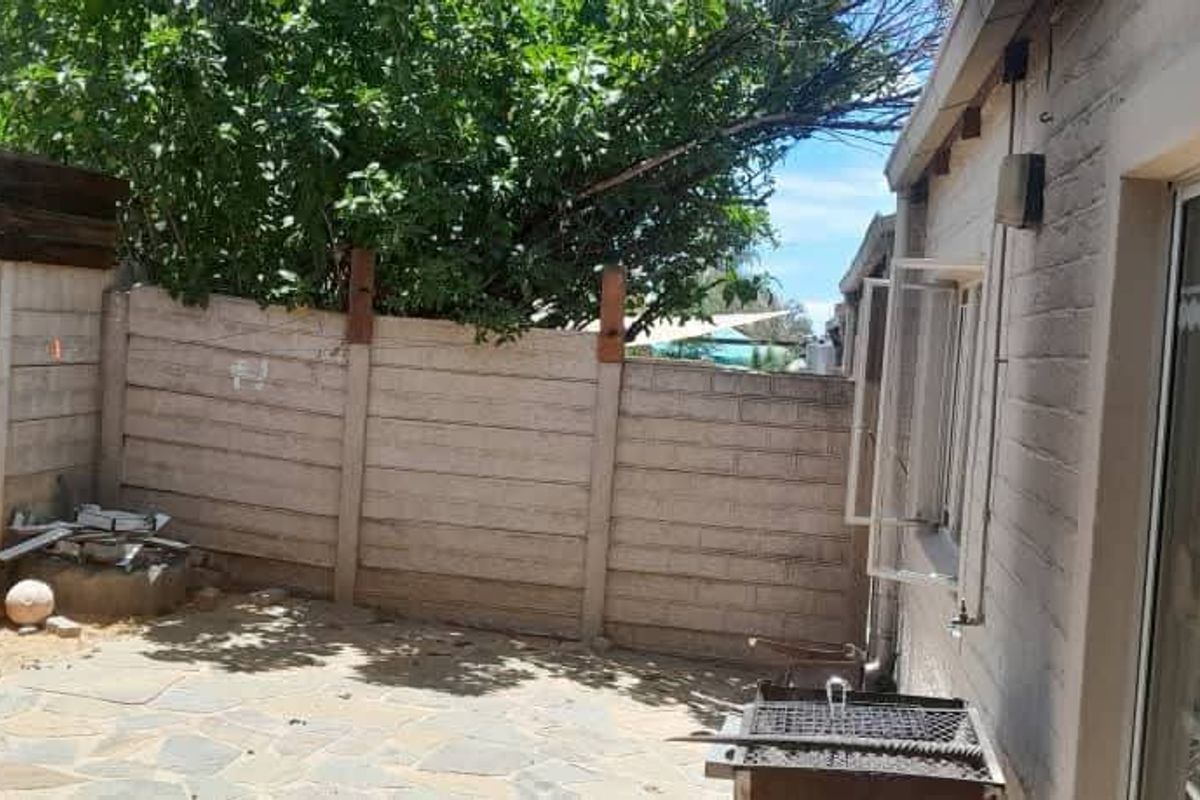 A private rear courtyard featuring a paved patio area, enclosed by precast concrete boundary walls and accessible via a sliding glass door.