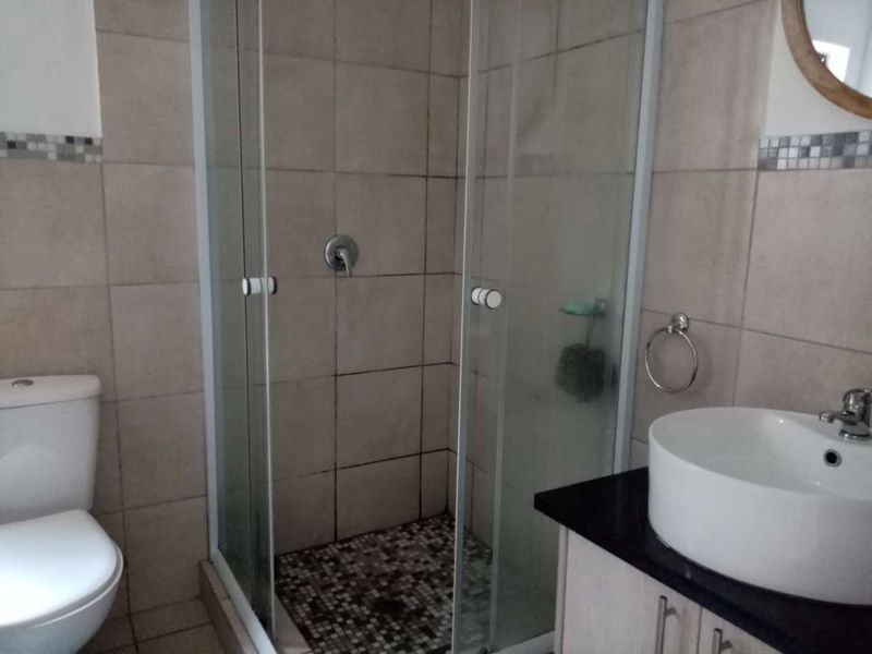 A functional bathroom featuring a glass-enclosed shower with mosaic flooring, a modern vessel sink on a vanity cabinet, and neutral wall tiling.