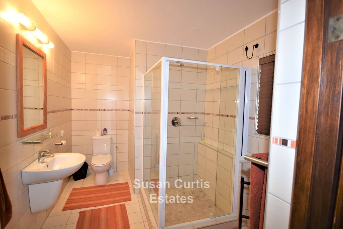 A functional bathroom featuring a glass-enclosed shower, pedestal basin, and toilet with neutral wall tiling.